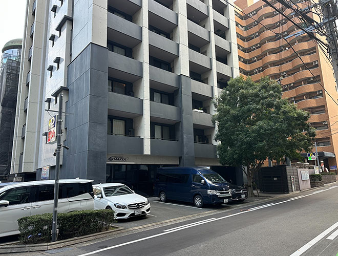 大きな木が立ってるグレーの建物の１F、ガラス張りのお店がマレア福岡博多です！